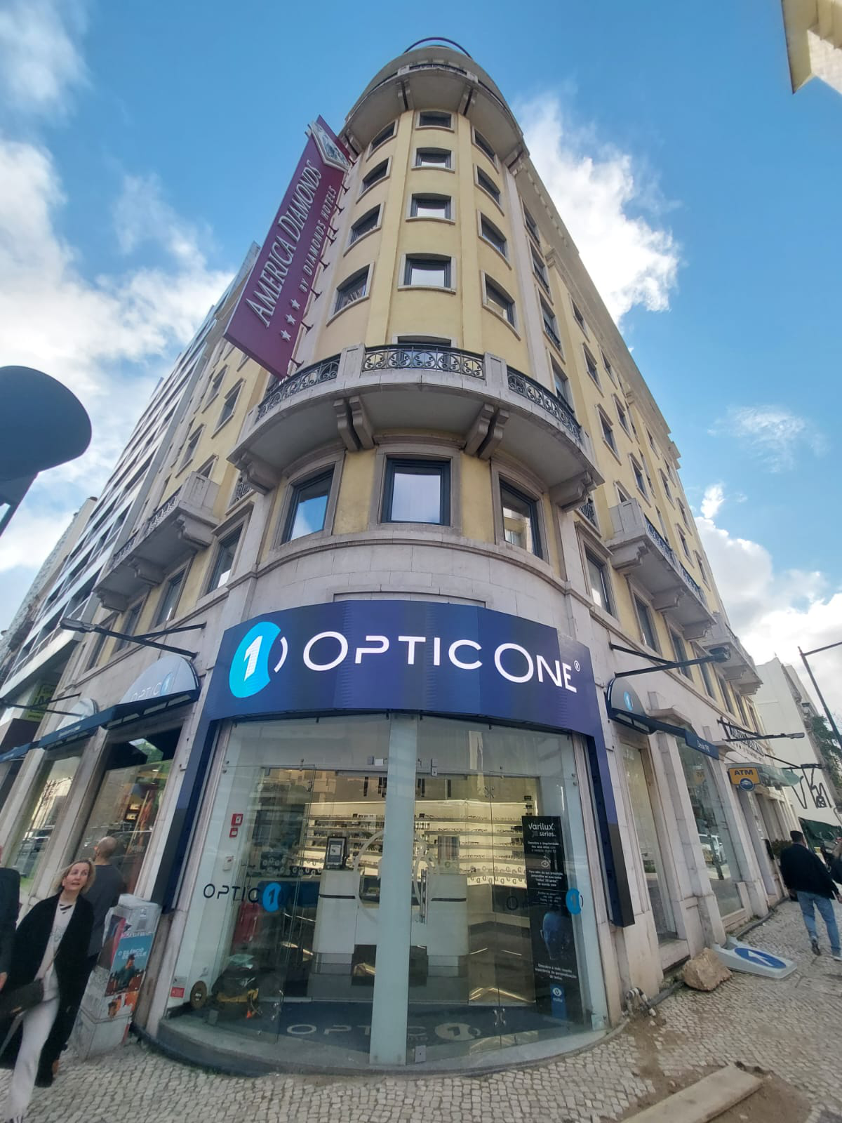 Ecrã LED exterior curvo Dynamic Screen instalado na fachada de canto de uma ótica Optic One em edifício histórico, para comunicação digital de alto impacto.